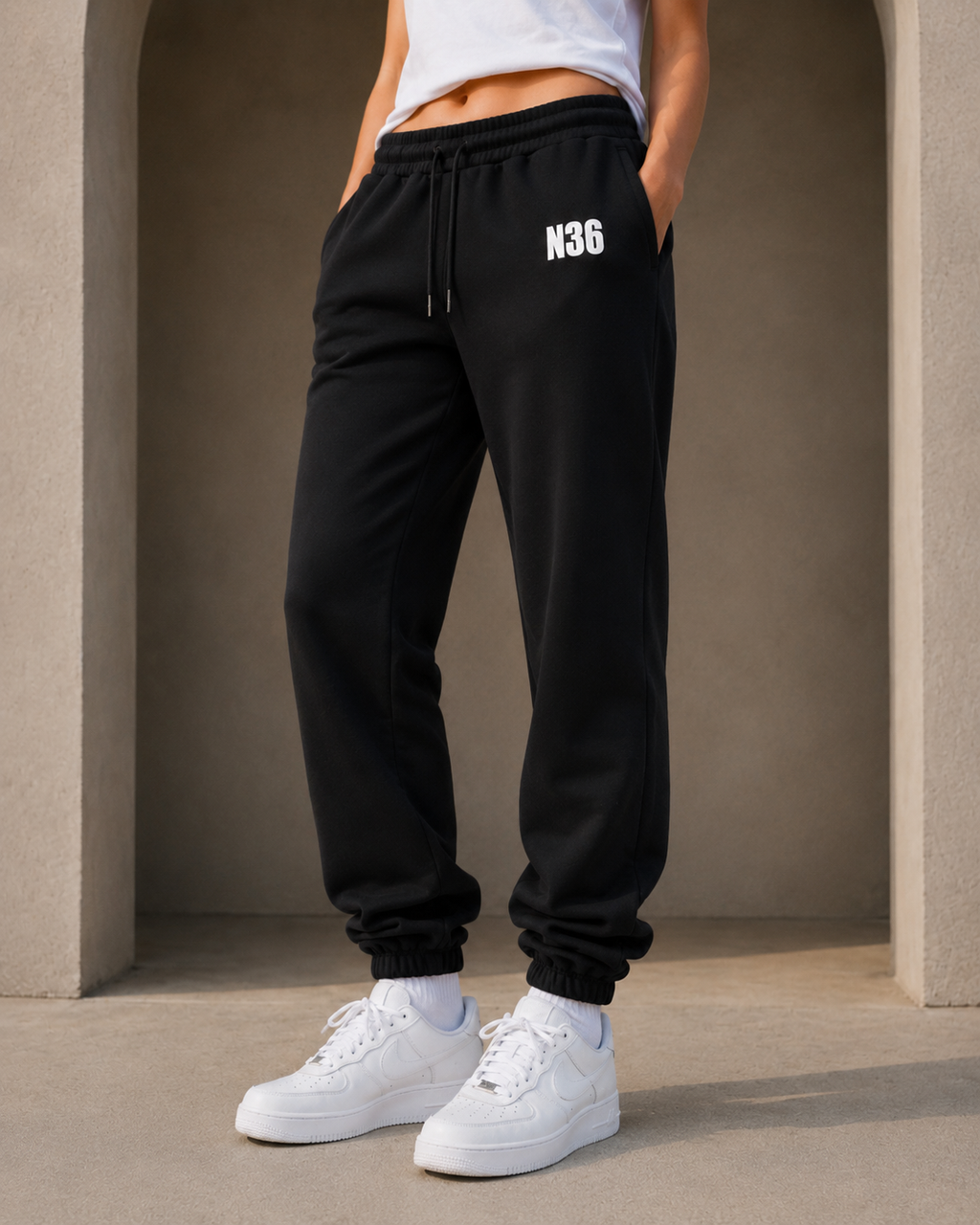 Person wearing black sweatpants with 'N36' logo and white sneakers in a neutral setting